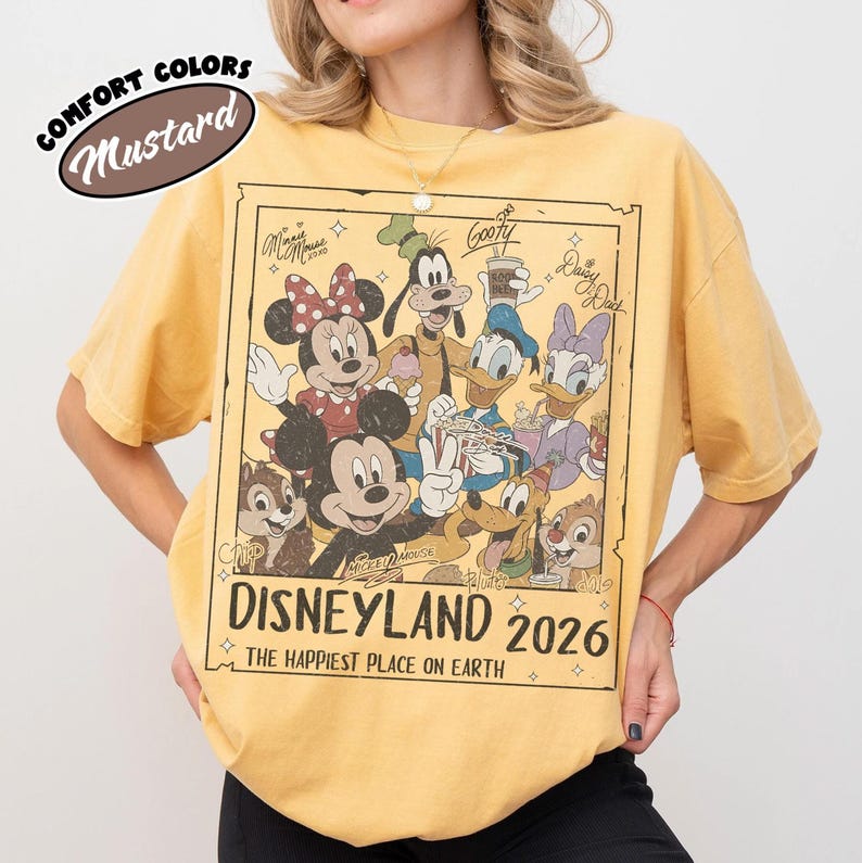 May include: Mustard-coloured t-shirt with a Disneyland 2026 graphic featuring Mickey Mouse, Minnie Mouse, Donald Duck, Goofy, and other Disney characters. The shirt has a vintage look with the words "Comfort Colors" above.