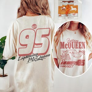 May include: Cream-colored t-shirt featuring a large red number "95" and the words "Lightning McQueen" in a stylized font. The back of the shirt displays the number "95" and the Lightning McQueen logo. The front of the shirt has a graphic of Lightning McQueen and the words "Think Fast".