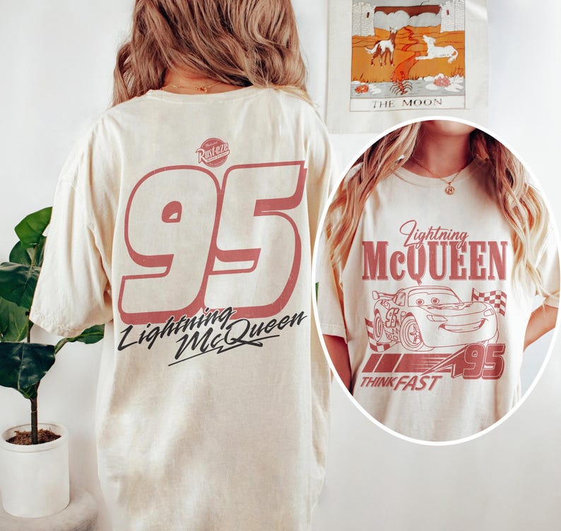 May include: Cream-colored t-shirt featuring a large red number "95" and the words "Lightning McQueen" in a stylized font. The back of the shirt displays the number "95" and the Lightning McQueen logo. The front of the shirt has a graphic of Lightning McQueen and the words "Think Fast".