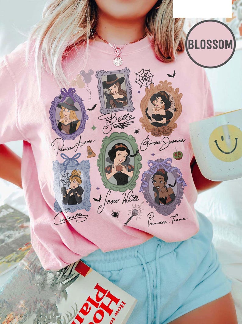 May include: Pink t-shirt featuring framed portraits of Disney princesses, including Belle, Aurora, Jasmine, Snow White, Cinderella, and Tiana. The shirt has a round "Blossom" logo and handwritten princess names.