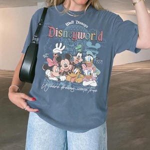 Puede incluir: Camiseta azul con un gr&aacute;fico de Disneyworld con Mickey Mouse, Minnie Mouse, Donald Duck, Goofy y Daisy Duck. La camiseta tiene el texto "Walt Disney's Disneyworld" y "Where dreams come true". El a&ntilde;o "1971" tambi&eacute;n est&aacute; impreso.