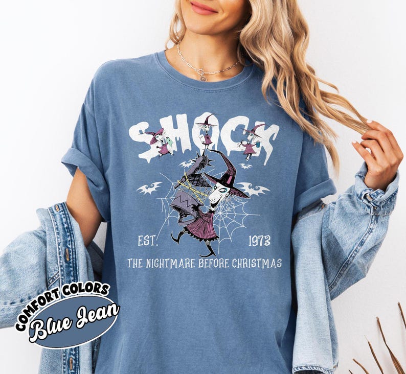 May include: Blue Comfort Colors t-shirt with a graphic from "The Nightmare Before Christmas." The design features the word "SHOCK" above a character in a witch hat and a spider web. The text "EST. 1973" and "THE NIGHTMARE BEFORE CHRISTMAS" are also included.