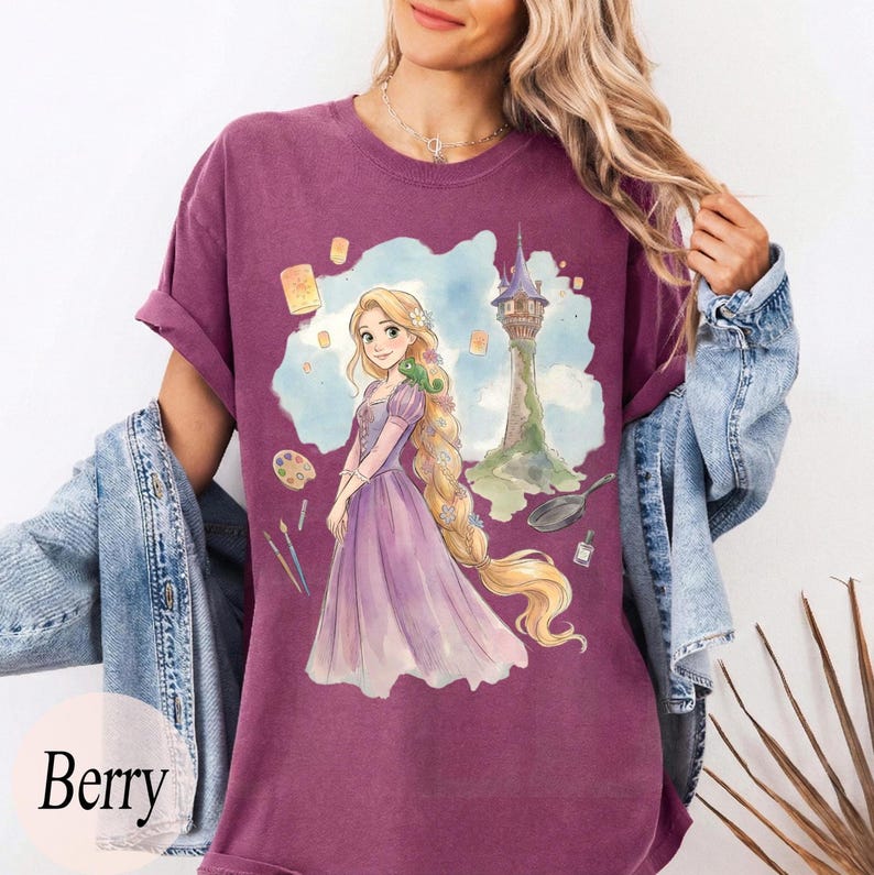 K&ouml;nnte beinhalten: Beerenfarbenes T-Shirt mit einer Aquarellillustration einer Prinzessin mit langem blondem Haar, einem Turm und schwebenden Laternen. Die Prinzessin tr&auml;gt ein lila Kleid. Das Wort "Berry" ist unten aufgedruckt.