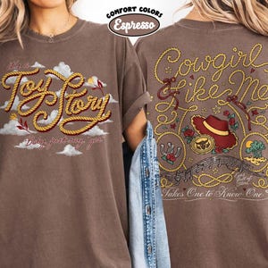 Może przedstawiać: Brązowy t-shirt z grafiką z przodu z napisem 'it's a Toy Story' wykonanym czcionką przypominającą linę wśr&oacute;d chmur oraz grafiką z tyłu z napisem 'Cowgirl like Me' i 'Takes One to Know One' z motywami kapelusza kowbojskiego i liny.