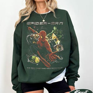 May include: Forest green Spider-Man sweatshirt. The graphic features Spider-Man in action with the text "SPIDER-MAN" above and "WITH GREAT POWER COMES GREAT RESPONSIBILITY" below. The sweatshirt is a crew neck style.