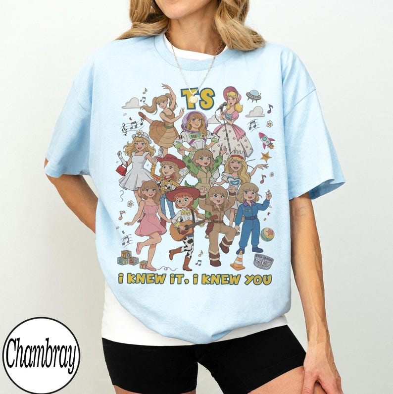 K&ouml;nnte beinhalten: Ein hellblaues T-Shirt mit einem Grafikdruck von mehreren Zeichentrickfiguren in verschiedenen Outfits, darunter ein Raumanzug und Cowgirl-Kleidung. Der Text "TS" steht oben und der Text "I KNEW IT, I KNEW YOU" ist unten aufgedruckt.