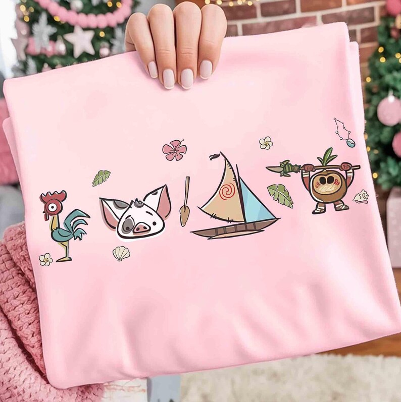 Pode incluir: Uma camisola rosa claro com uma impress&atilde;o gr&aacute;fica de um galo de desenho animado, uma cara de porco, um remo de madeira, um pequeno veleiro com vela estampada e uma personagem de coco com uma lan&ccedil;a, com pequenas flores e folhas tropicais.