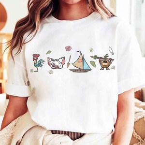 Pode incluir: Uma t-shirt branca de manga curta com uma impress&atilde;o gr&aacute;fica horizontal de um galo de desenho animado, uma cara de porco, um remo de madeira, um veleiro com vela estampada e uma pequena criatura de coco com uma lan&ccedil;a, decorada com flores.