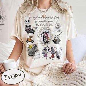 Pu&ograve; includere: T-shirt color avorio con una grafica di "Nightmare Before Christmas". Il design include personaggi come Jack Skellington, Sally e altri, con il testo "The Nightmare Before Christmas, The Pumpkin Queen, The Pumpkin King."