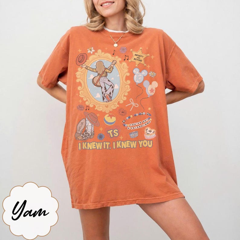 May include: An orange short-sleeve t-shirt featuring a graphic print with a central oval frame containing a figure playing a guitar, surrounded by various icons including balloons, a cowboy boot, and text reading "INFINITY AND BEYOND", "YOU'VE GOT A FRIEND IN ME", "TS", and "I KNEW IT, I KNEW YOU".
