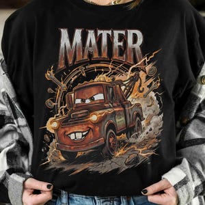 May include: Black t-shirt featuring a cartoon illustration of Mater from the movie Cars. The design includes the word "MATER" in large, distressed lettering above the character, with lightning bolts and tools surrounding the truck.