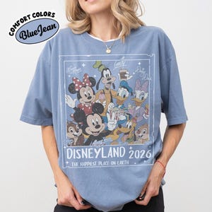 May include: Blue t-shirt with a graphic featuring Disney characters, including Mickey and Minnie Mouse, Goofy, Donald Duck, and Daisy Duck. The graphic reads "Disneyland 2026" and "The Happiest Place on Earth."