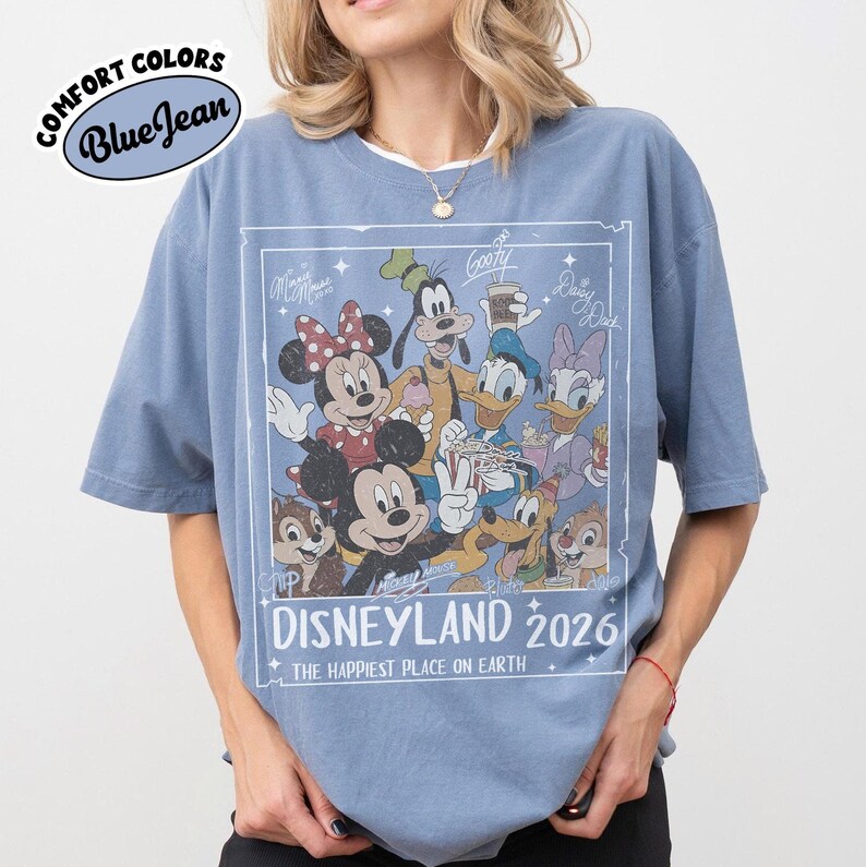 May include: Blue t-shirt with a graphic featuring Disney characters, including Mickey and Minnie Mouse, Goofy, Donald Duck, and Daisy Duck. The graphic reads "Disneyland 2026" and "The Happiest Place on Earth."