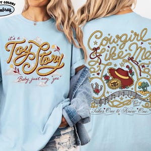Może przedstawiać: Jasnoniebieski t-shirt z grafiką z przodu przedstawiającą ż&oacute;łty napis w stylu liny o treści "it's a Toy Story" i "Baby, just say 'yes'". Grafika z tyłu zawiera napis "Cowgirl like Me" z liny, czerwony kapelusz kowbojski oraz "Takes One to Know One".