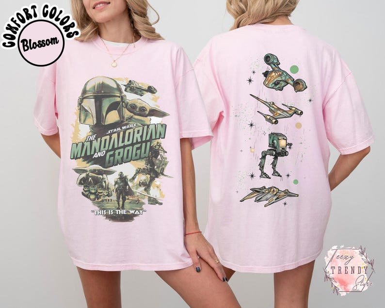 Pode incluir: Uma t-shirt rosa claro com uma impress&atilde;o gr&aacute;fica de The Mandalorian e Grogu na frente, incluindo o texto "The Mandalorian and Grogu" e "This is the way". As costas da t-shirt exibem um alinhamento vertical de quatro ve&iacute;culos Star Wars.