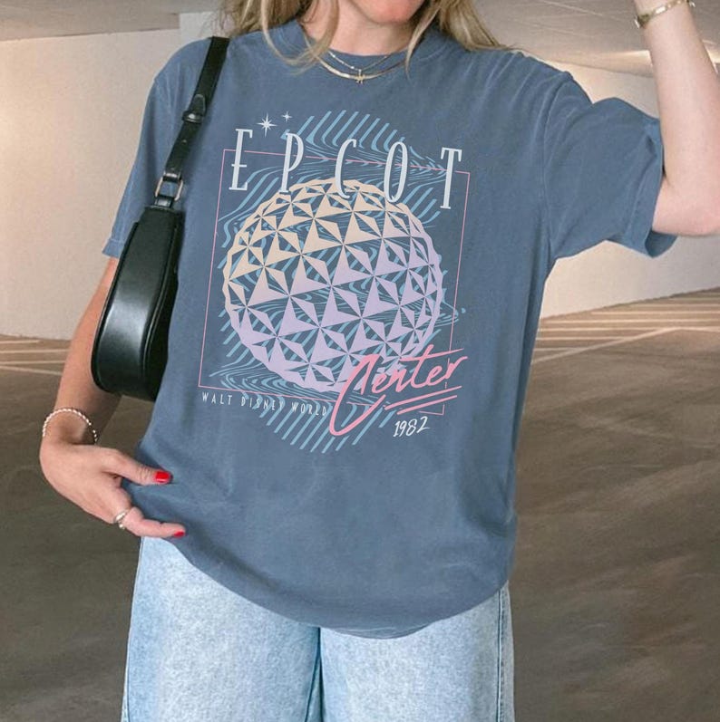 May include: A blue t-shirt featuring the text "EPCOT" above a geometric sphere design with pastel colors. Below the sphere, the text "Verter 1982" is displayed. The shirt also includes the text "WALT DISNEY WORLD".