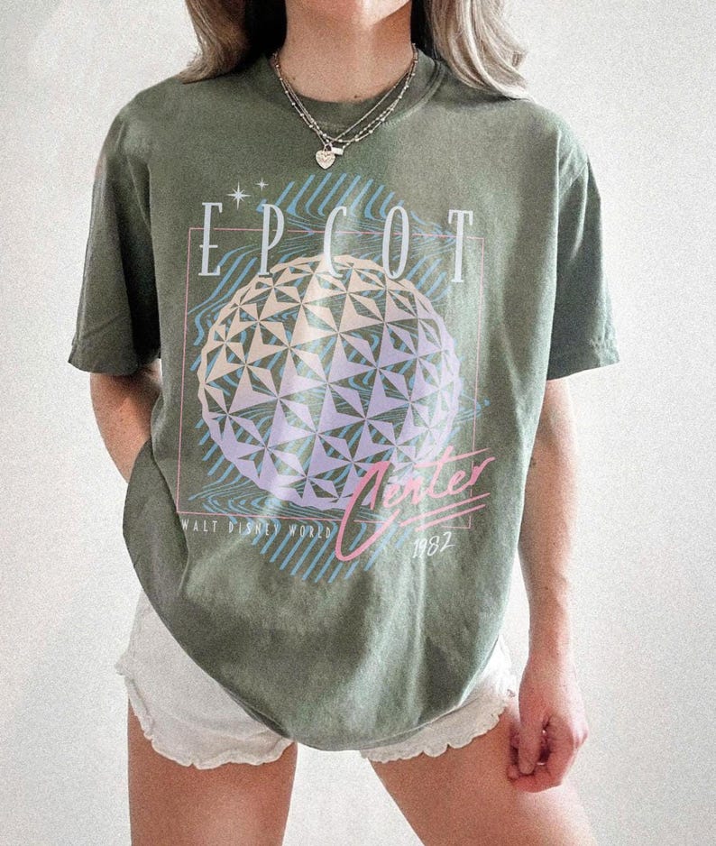 May include: Olive green t-shirt featuring the text "EPCOT Center" above a geometric sphere design in shades of purple and blue. The shirt also includes the text "Winter 1982" and "Walt Disney World".