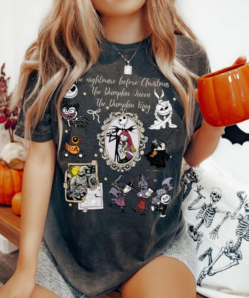 Pu&ograve; includere: T-shirt grigio scuro con personaggi e testo di "Nightmare Before Christmas". Il design include Jack Skellington e Sally in una cornice ovale, insieme ad altri personaggi e le frasi "The Pumpkin Queen" e "The Pumpkin King".