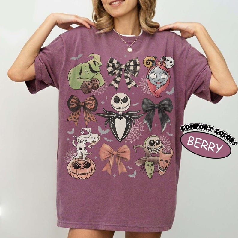 May include: A berry-colored short-sleeve t-shirt featuring a graphic print of characters from The Nightmare Before Christmas, including Jack Skellington, Sally, and Oogie Boogie, interspersed with various bows and spiderweb patterns.