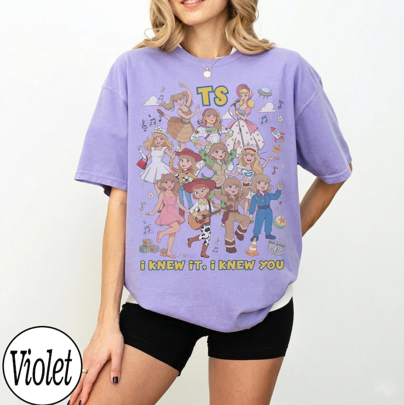 K&ouml;nnte beinhalten: Ein hellviolettes Kurzarm-T-Shirt mit einem Grafikdruck von mehreren Zeichentrickfiguren in verschiedenen Outfits. Der Text TS ist oben aufgedruckt und der Text i knew it, i knew you steht unten in gelben Buchstaben auf dem T-Shirt.