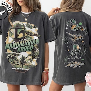Pode incluir: Uma t-shirt cinzento-carv&atilde;o de manga curta com uma impress&atilde;o gr&aacute;fica de The Mandalorian e Grogu na frente, com o texto "The Mandalorian and Grogu" e "This is the way". As costas apresentam quatro ve&iacute;culos de Star Wars alinhados verticalmente.