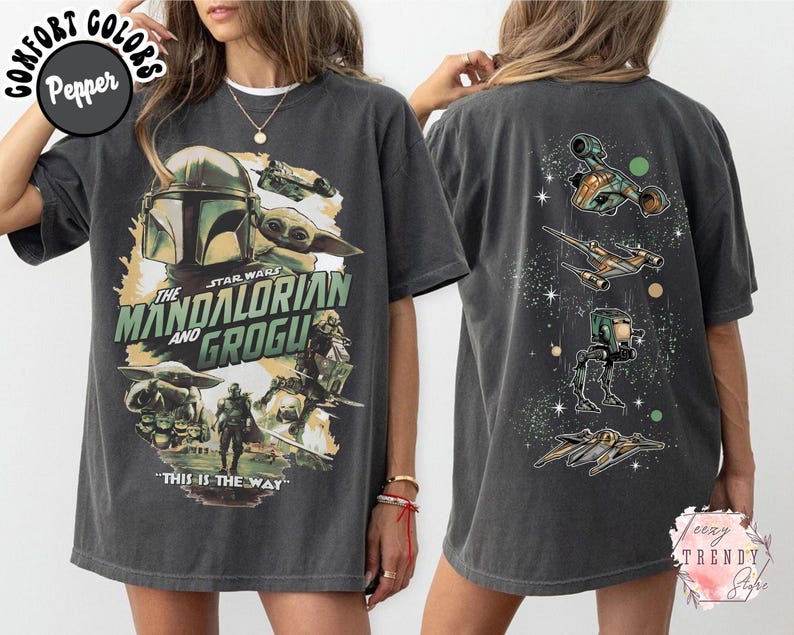 Pode incluir: Uma t-shirt cinzento-carv&atilde;o de manga curta com uma impress&atilde;o gr&aacute;fica de The Mandalorian e Grogu na frente, com o texto "The Mandalorian and Grogu" e "This is the way". As costas apresentam quatro ve&iacute;culos de Star Wars alinhados verticalmente.