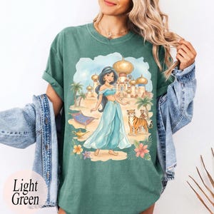 K&ouml;nnte beinhalten: Hellgr&uuml;nes T-Shirt mit einem Aufdruck einer Prinzessin in einem blauen Kleid, einem Tiger, einem fliegenden Teppich und einem Palast. Die Worte "Light Green" sind unten links auf dem T-Shirt aufgedruckt.