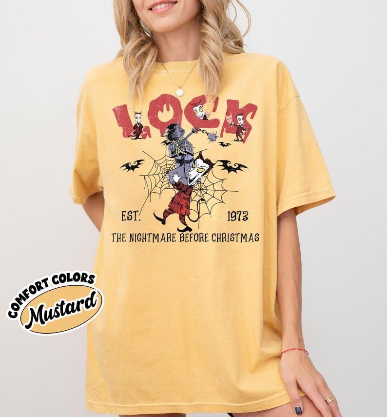 May include: Mustard-colored t-shirt featuring a graphic from "The Nightmare Before Christmas." The design includes the word "Lock" in red, along with characters and the text "EST. 1973." The shirt has a relaxed fit.