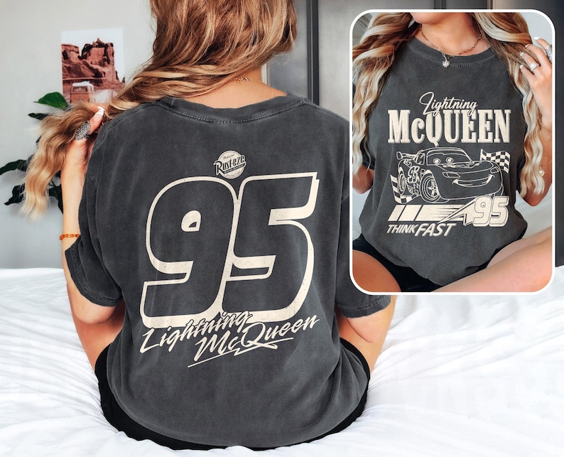 May include: Dark gray t-shirt featuring the number 95 in a large, off-white font on the back, with "Lightning McQueen" below. The front of the shirt has a graphic of Lightning McQueen with the text "Lightning McQueen", "Think Fast", and the number 95.