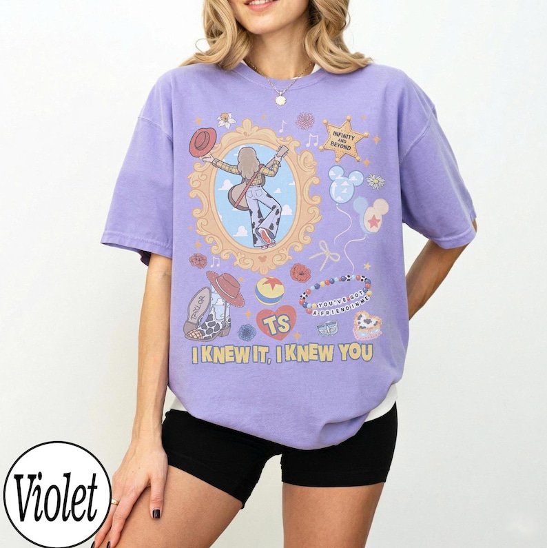 May include: A violet short-sleeve t-shirt featuring a graphic print of a person in a mirror, a cowboy boot, a ball, a star, and balloons. The text reads "INFINITY AND BEYOND", "YOU'VE GOT A FRIEND IN ME", "TS", and "I KNEW IT, I KNEW YOU".