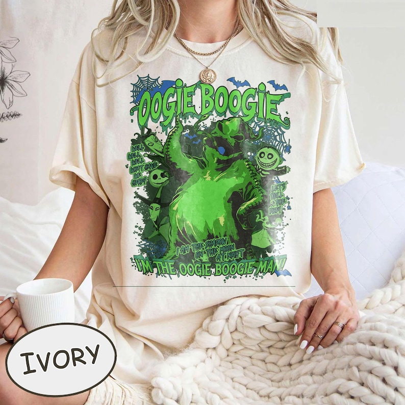 Op de afbeelding: Ivoor T-shirt met een groene afbeelding van Oogie Boogie uit The Nightmare Before Christmas. Het ontwerp bevat de tekst "Oogie Boogie" en "I'm the Oogie Boogie Man!" in een griezelig lettertype. Het shirt heeft een relaxte pasvorm.