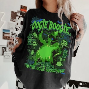 Op de afbeelding: Donkergrijs t-shirt met een groene afbeelding van Oogie Boogie uit The Nightmare Before Christmas. Het ontwerp bevat de tekst "Oogie Boogie" en "I'm the Oogie Boogie Man!" met andere personages.