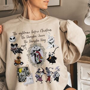 Pu&ograve; includere: Felpa beige con personaggi e testo da "Nightmare Before Christmas". Il design include Jack Skellington, Sally e altri personaggi. Il testo recita "The Nightmare Before Christmas, The Pumpkin Queen, The Pumpkin King."