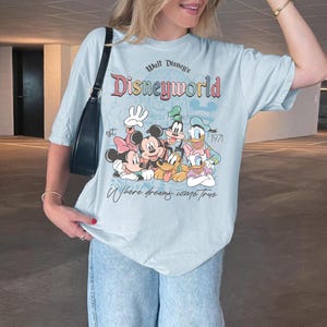 Puede incluir: Camiseta azul claro con un gr&aacute;fico de Disney World con Mickey Mouse, Minnie Mouse, Donald Duck, Goofy y Daisy Duck. La camiseta tiene el texto "Walt Disney's Disneyworld" y "Where dreams come true."