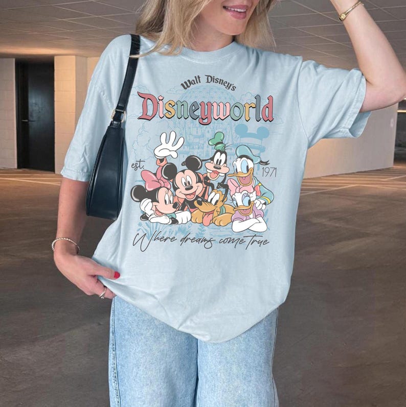 Puede incluir: Camiseta azul claro con un gr&aacute;fico de Disney World con Mickey Mouse, Minnie Mouse, Donald Duck, Goofy y Daisy Duck. La camiseta tiene el texto "Walt Disney's Disneyworld" y "Where dreams come true."