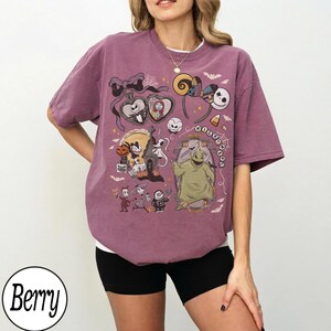 Może przedstawiać: Jagodowy t-shirt z kr&oacute;tkim rękawem z nadrukiem graficznym przedstawiającym postacie i motywy z Miasteczka Halloween, w tym Jacka Skellingtona, Sally, Oogie Boogie i Zero, z tekstem "NIGHTMARE" wkomponowanym w projekt.