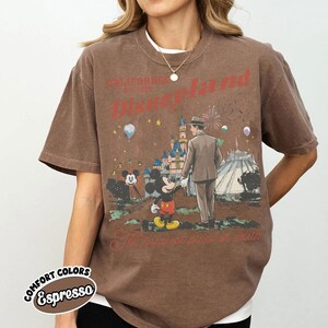 Puede incluir: Camiseta color espresso con un gr&aacute;fico de Disneyland. El dise&ntilde;o incluye a Mickey Mouse, un hombre con traje, un castillo y el texto "California Disneyland Est. 1955". La camiseta tambi&eacute;n tiene las palabras "The happiest place on earth".