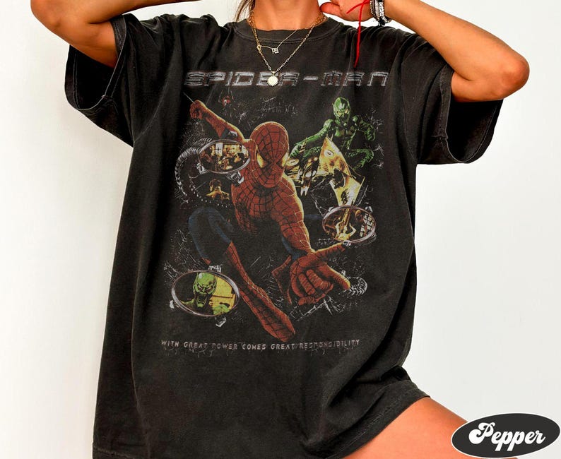 May include: Black t-shirt featuring a Spider-Man graphic. The design includes Spider-Man in action, along with the Green Goblin. The text "SPIDER-MAN" is at the top, and "WITH GREAT POWER COMES GREAT RESPONSIBILITY" is at the bottom.