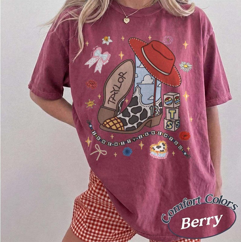 May include: A berry-colored short-sleeve t-shirt featuring a graphic print of a cowboy boot with a cow print pattern, a red cowboy hat, a bow, and blocks with the letters T, S, and 13. The text TAYLOR and I KNEW YOU are printed on the shirt.