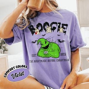 May include: A violet t-shirt featuring the word "Boogie" in a dripping font, with cartoon characters and the text "EST. 1973 THE NIGHTMARE BEFORE CHRISTMAS." A comfort colors label reads "Violet."