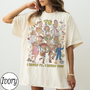 K&ouml;nnte beinhalten: Ein elfenbeinfarbenes Kurzarm-T-Shirt mit einem Grafikdruck von mehreren Zeichentrickfiguren in verschiedenen Outfits. Der Text TS ist oben aufgedruckt und der Text I KNEW IT, I KNEW YOU ist unten in gelben Gro&szlig;buchstaben aufgedruckt.