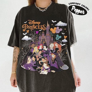May include: A charcoal gray t-shirt featuring a graphic print of Disney Princesses in Halloween costumes in front of a castle. The text reads Disney Princess and Comfort Colors Pepper. The design includes bats, spiderwebs, and Mickey-shaped balloons.