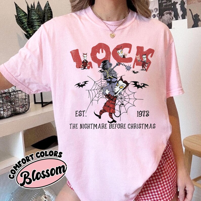 May include: Pink t-shirt with a graphic from "The Nightmare Before Christmas." The design features the word "LOCK" in red, along with characters, bats, and a spiderweb. The text "EST. 1973" and "THE NIGHTMARE BEFORE CHRISTMAS" are also included.