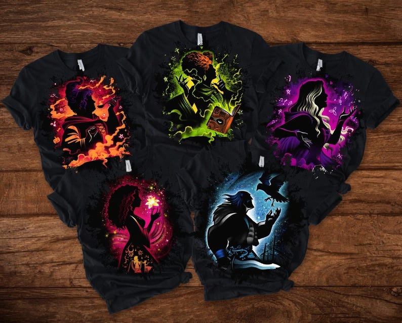 May include: Five black t-shirts with colorful graphic designs. Each shirt features a silhouette of a person with magical elements. The designs include flames, glowing books, and mystical figures. The shirts are displayed on a wooden surface.