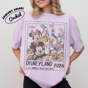 May include: Orchid-coloured t-shirt with a Disneyland 2026 graphic, featuring Mickey Mouse, Minnie Mouse, Goofy, Donald Duck, Daisy Duck, Chip, and Dale. The shirt has a vintage design and the text "The Happiest Place on Earth."