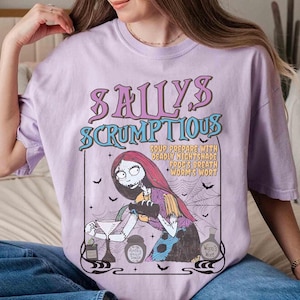May include: A light purple t-shirt featuring a graphic of Sally from The Nightmare Before Christmas. The graphic includes the text "Sally's Scrumptious" and a recipe. The design is in shades of purple, teal, and black.