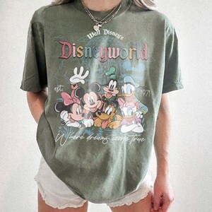 Puede incluir: Camiseta verde oliva con un gr&aacute;fico de Disney World con Mickey Mouse, Minnie Mouse, Donald Duck y Goofy. La camiseta tiene el texto "Walt Disney's Disneyworld" y "Where dreams come true."