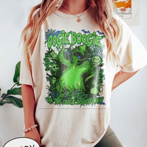 Op de afbeelding: Ivoor T-shirt met een groene afbeelding van het personage Oogie Boogie, met de tekst "Oogie Boogie" en "I'm the Oogie Boogie Man!" Het ontwerp bevat vleermuizen en andere personages uit de film.