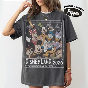 May include: Dark grey t-shirt with a graphic featuring Disney characters such as Mickey Mouse, Minnie Mouse, Goofy, Donald Duck, and Daisy Duck. The graphic includes the text "Disneyland 2026" and "The Happiest Place on Earth."