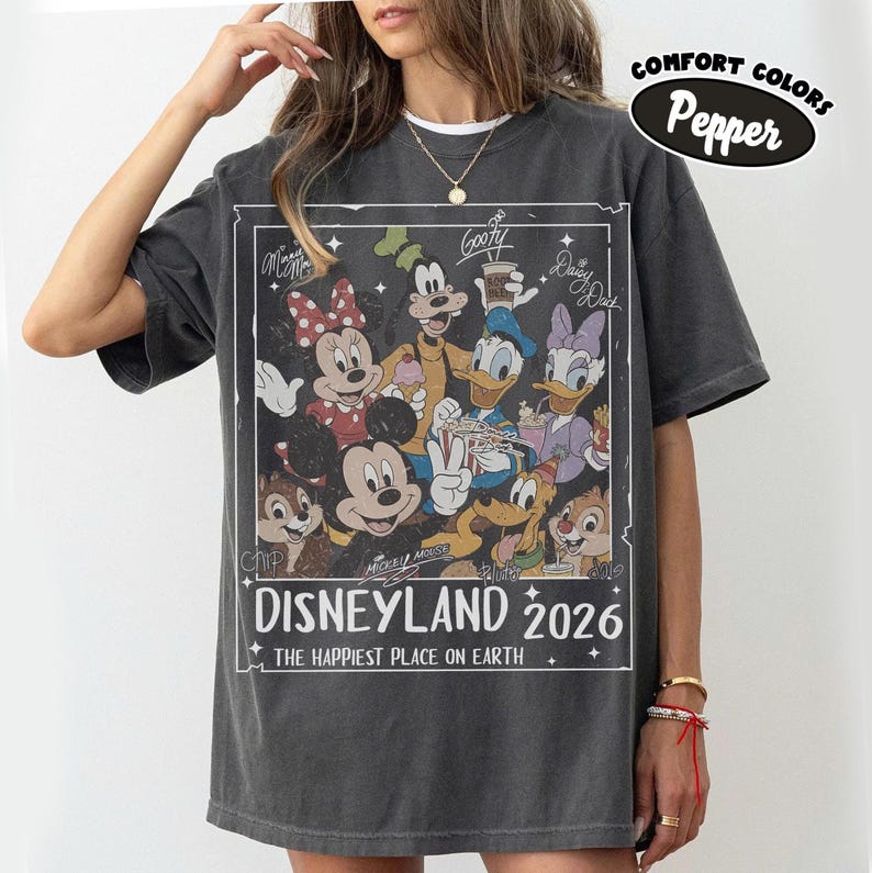 May include: Dark grey t-shirt with a graphic featuring Disney characters such as Mickey Mouse, Minnie Mouse, Goofy, Donald Duck, and Daisy Duck. The graphic includes the text "Disneyland 2026" and "The Happiest Place on Earth."
